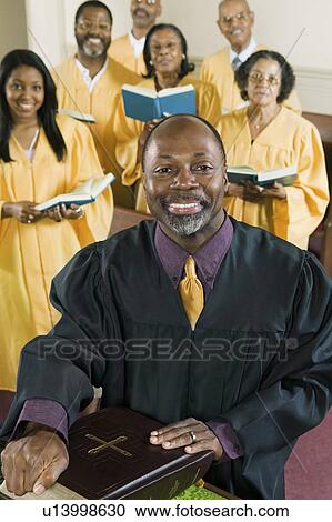 Stock Image - Minister at altar with Bible, gospel choir in background, portrait. Fotosearch