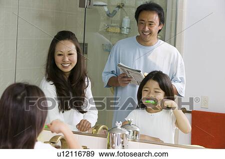Stock Photo - Mirror reflection of Family in Bathroom Getting Ready for Day, daughter brushing teeth. Fotosearch