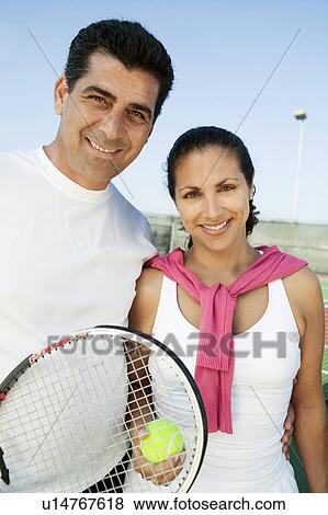 Stock Photo - Mixed doubles Tennis Players standing on tennis court, portrait. Fotosearch