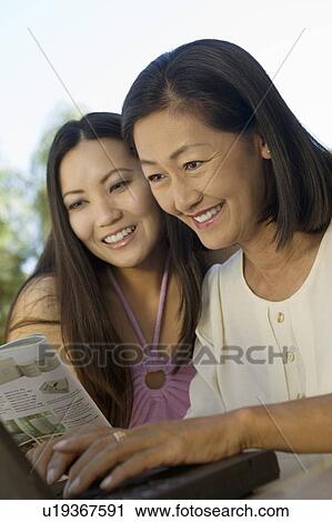 Stock Image - Mother and Daughter sitting at backyard table Using Laptop Together. Fotosearch