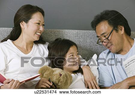 Picture - Mother and father relaxing in bed with daughter. Fotosearch