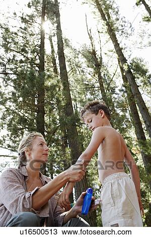Stock Image - Mother Applying Suntan Lotion to Son (7-9), low angle view.. Fotosearch
