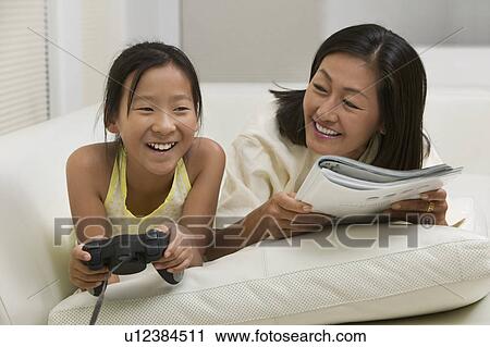 Mother reading on couch with Daughter Playing Video Game, front view View Large Photo Image Stock Image - Mother reading on couch with Daughter Playing Video Game, front view. Fotosearch