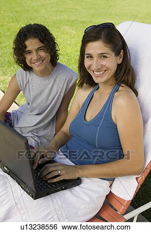 Mother sitting on sunlounger, Using Laptop Outdoors with son (13-15), portrait. View Large Photo Image Stock Photograph - Mother sitting on sunlounger, Using Laptop Outdoors with son (13-15), portrait.. Fotosearch