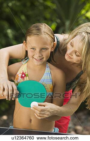 Stock Image - Mother teaching daughter (5-7) to play ping-pong, outdoors.. Fotosearch
