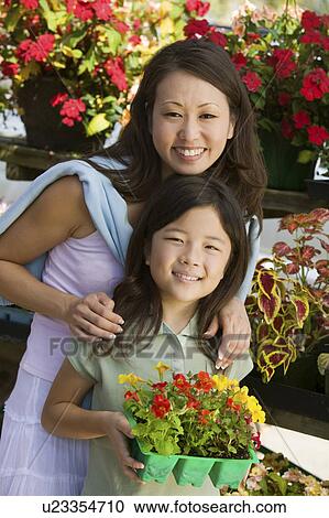 Stock Image - Mother with daughter holding young flowers in plant nursery, portrait. Fotosearch