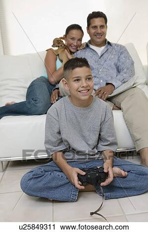Stock Image - Parents Watching Son Play Video Games in living room, front view. Fotosearch