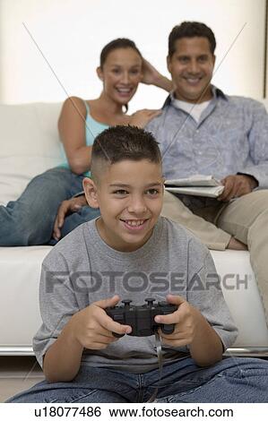 Stock Photograph - Parents Watching Son Play Video Games in living room, front view. Fotosearch