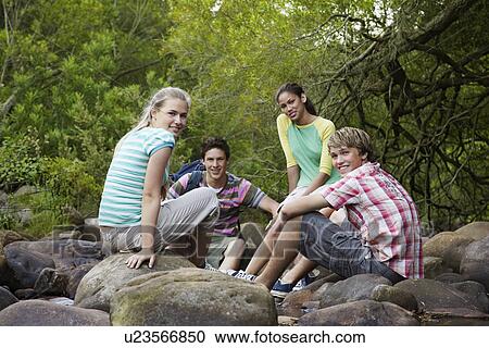 Portrait of four teenagers (16-17 years) sitting on stones by river, smiling View Large Photo Image Stock Image - Portrait of four teenagers (16-17 years) sitting on stones by river, smiling. Fotosearch