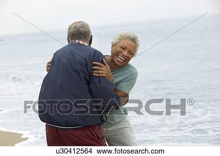 Picture - Senior couple embracing by ocean. Fotosearch