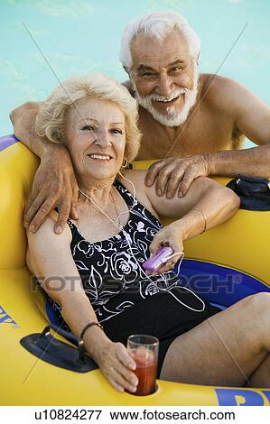 Senior Couple in Swimming Pool, woman lying on inflatable raft, holding drink, listening to portable music player, portrait. View Large Photo Image Stock Photo - Senior Couple in Swimming Pool, woman lying on inflatable raft, holding drink, listening to portable music player, portrait.. Fotosearch