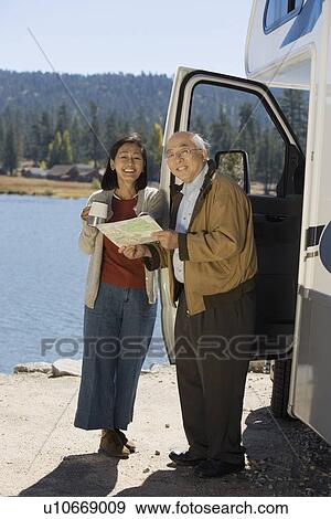Stock Photo - Senior couple looking at map outside RV at lake. Fotosearch
