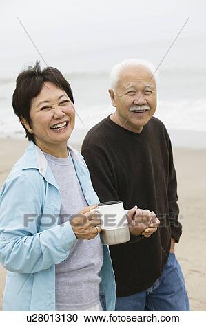 Senior couple on beach holding hands and looking at camera View Large Photo Image Stock Image - Senior couple on beach holding hands and looking at camera. Fotosearch