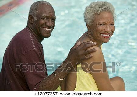 Stock Photo - Senior Couple sitting by swimming pool, portrait.. Fotosearch