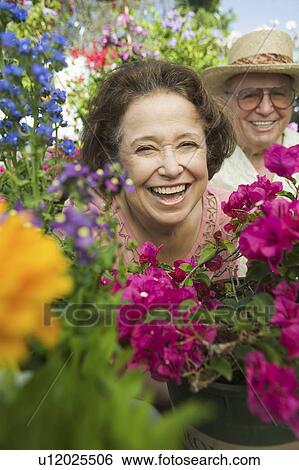 Stock Photograph - Senior Couple sitting in plant nursery seen through bed of flowers, portrait. Fotosearch