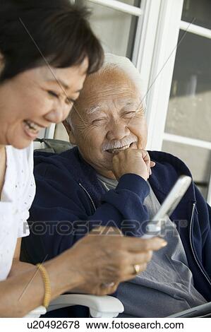 Stock Photo - Senior couple using mobile phone, smiling, outdoors. Fotosearch