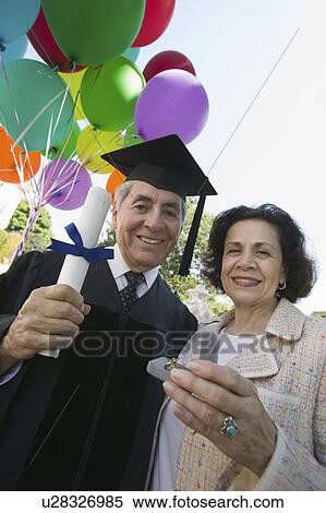 Senior graduate receiving present from wife outside, low angle view View Large Photo Image Stock Photography - Senior graduate receiving present from wife outside, low angle view. Fotosearch