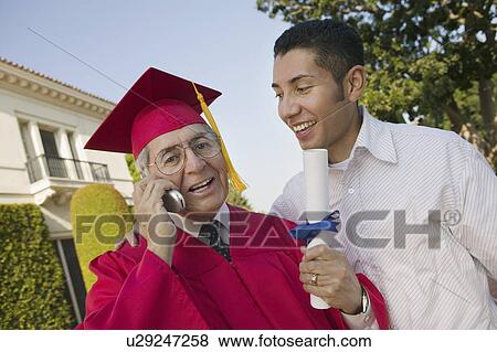 Stock Photo - Senior Graduate using cell phone outside with son, low angle view. Fotosearch