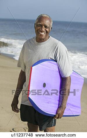 Stock Photo - Senior man holding surfboard. Fotosearch