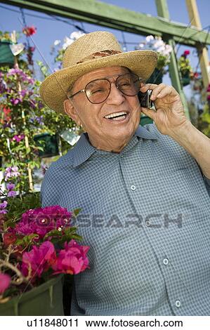 Stock Image - Senior Man standing in plant nursery Using Cell Phone. Fotosearch
