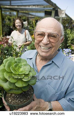 Senior man standing in plant nursery holding cactus plant, portrait View Large Photo Image Stock Image - Senior man standing in plant nursery holding cactus plant, portrait. Fotosearch