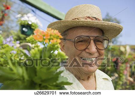 Stock Image - Senior Man standing in plant nursery, portrait, close up. Fotosearch