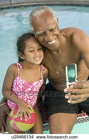 Picture - Senior man using mobile phone, photographing self with granddaughter (5-6) at swimming pool.. Fotosearch