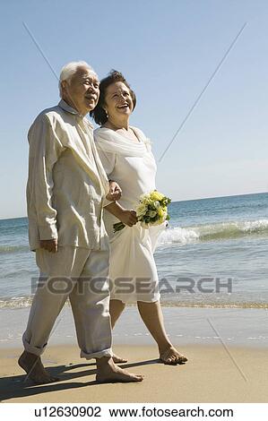 Senior newly weds walking arm in arm on beach View Large Photo Image Stock Image - Senior newly weds walking arm in arm on beach. Fotosearch
