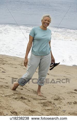 Stock Photo - Senior woman standing barefoot on beach, (portrait). Fotosearch