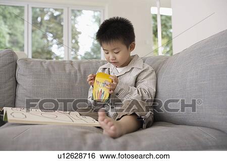 Stock Photograph - Smiling Boy on sitting barefooted on Sofa with Coloring Book. Fotosearch