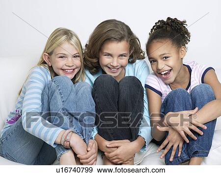 Stock Photo - Smiling Friends sitting side by side, knees tucked. Fotosearch