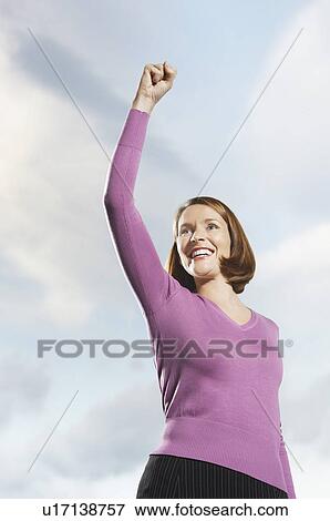 Stock Photo - Smiling mid-adult woman standing outside, arm raised. Fotosearch