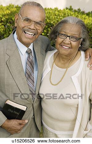 Stock Photograph - Smiling Senior Christian Couple in garden holding Bible, portrait. Fotosearch