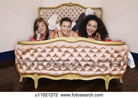 Stock Image - Smiling Teenage Girls lying on funky cushion bed. Fotosearch