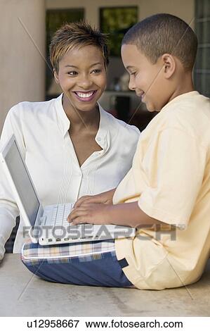 Son sitting on counter in living room using laptop with mother, side view View Large Photo Image Stock Photo - Son sitting on counter in living room using laptop with mother, side view. Fotosearch