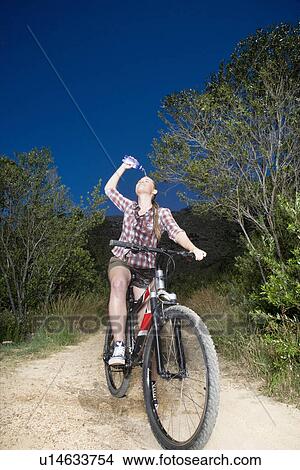Teenage girl (16-17 years) on bike on dirt road, spilling water over face View Large Photo Image Picture - Teenage girl (16-17 years) on bike on dirt road, spilling water over face. Fotosearch