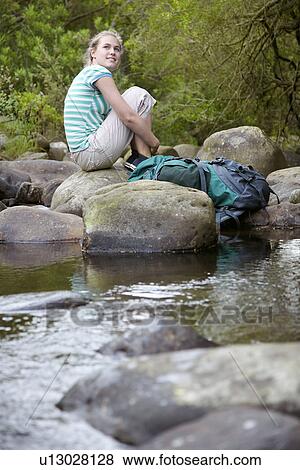Stock Photo - Teenage girl (16-17 years) sitting on stone by river, looking up. Fotosearch