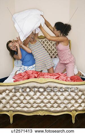 Stock Image - Teenage Girls pillow fighting, kneeling on funky bed. Fotosearch