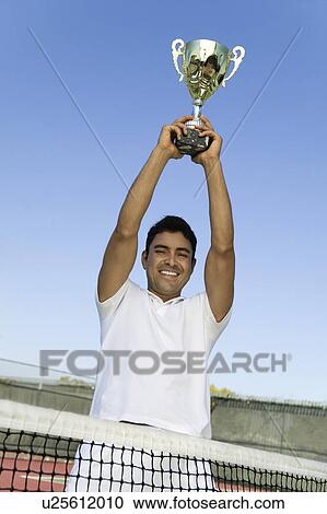 Stock Image - Tennis Player on court by net Holding Trophy Over Head, portrait. Fotosearch
