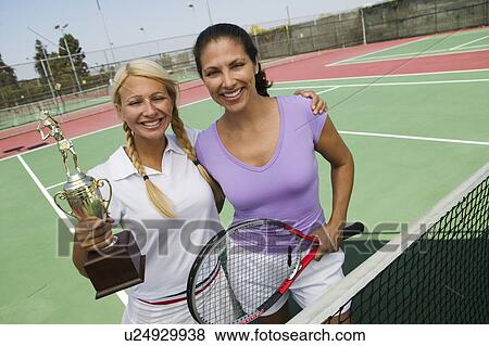 Stock Photo - Two female Tennis Players by net on court holding trophy, portrait. Fotosearch