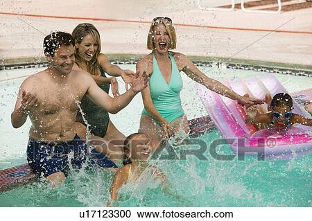Stock Image - Two girls (7-9) playing with family in swimming pool.. Fotosearch