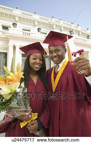 Stock Photo - Two graduates holding diploma and flowers outside university, portrait. Fotosearch