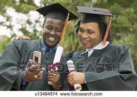 Two graduates looking at cell phone outside, low angle view View Large Photo Image Picture - Two graduates looking at cell phone outside, low angle view. Fotosearch