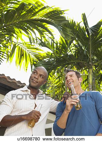 Stock Image - Two men having conversation outdoors, low angle view. Fotosearch