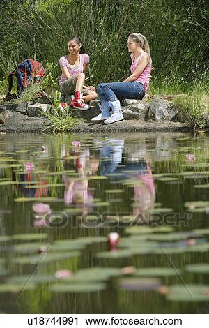 Two teenage girls (16-17 years) sitting on stones by lake, smiling View Large Photo Image Stock Image - Two teenage girls (16-17 years) sitting on stones by lake, smiling. Fotosearch