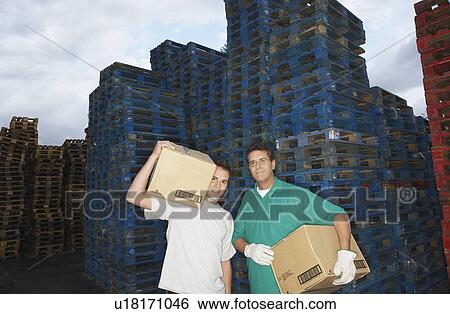 Warehouse Workers Carrying Boxes in front of stacks of pallets View Large Photo Image Stock Photograph - Warehouse Workers Carrying Boxes in front of stacks of pallets. Fotosearch