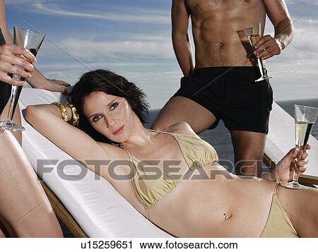 Woman in bikini holding champagne glass with man and woman standing near ocean View Large Photo Image Stock Image - Woman in bikini holding champagne glass with man and woman standing near ocean. Fotosearch