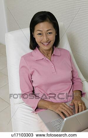 Stock Image - Woman in Chair Using Laptop, portrait, high angle view. Fotosearch