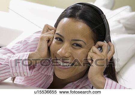 Stock Photography - Woman lying on sofa Listening to Music on headphones, portrait. Fotosearch