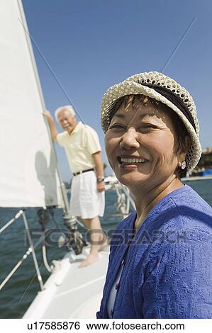 Stock Photograph - Woman smiling on sailboat, husband in background, (portrait). Fotosearch